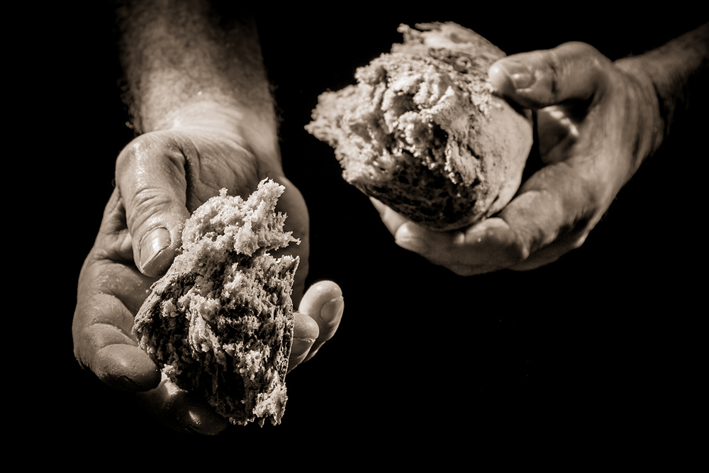 Hands offer a piece of broken bread (Dreamstime/Shaiith)