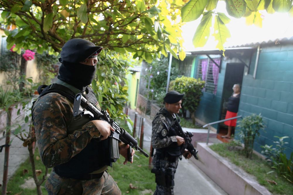 A woman stands in a doorway while armed Salvadoran troops patrol a residential area in Soyapango on Dec. 5, 2022. (CNS/Reuters/José Cabezas)