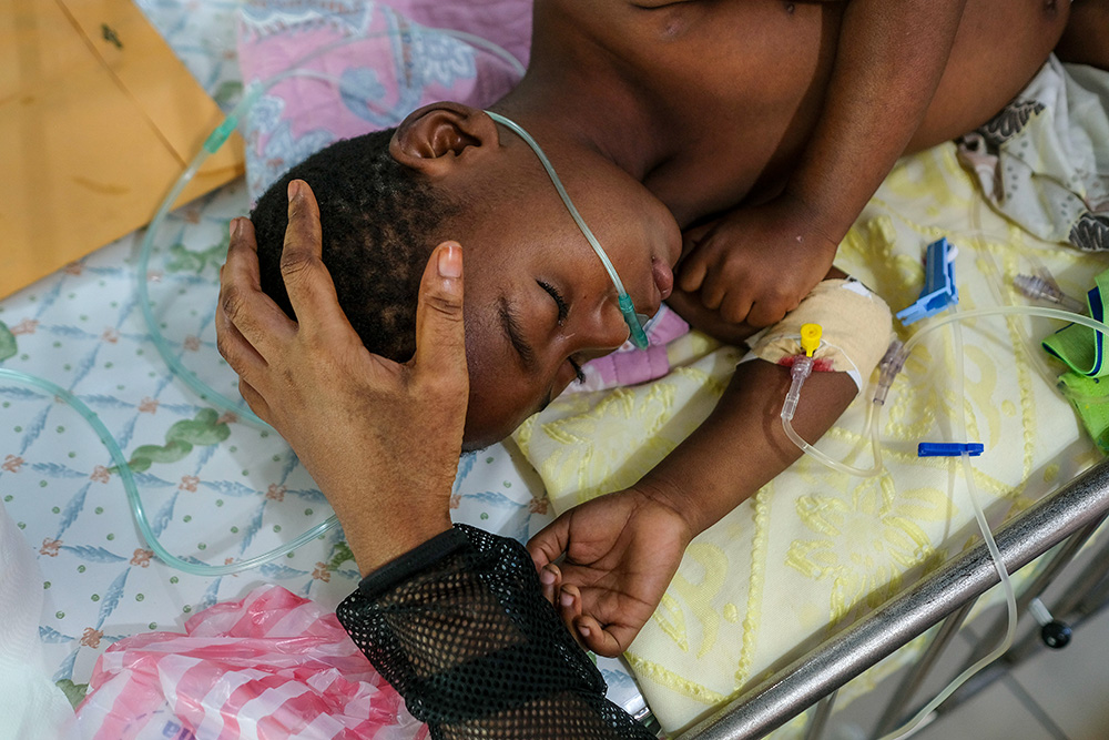 A woman caresses her child's head as he rests on a bed at the St. Damien Pediatric Hospital of Port-au-Prince, Haiti, Friday, Nov. 12, 2021. (AP/Matias Delacroix)
