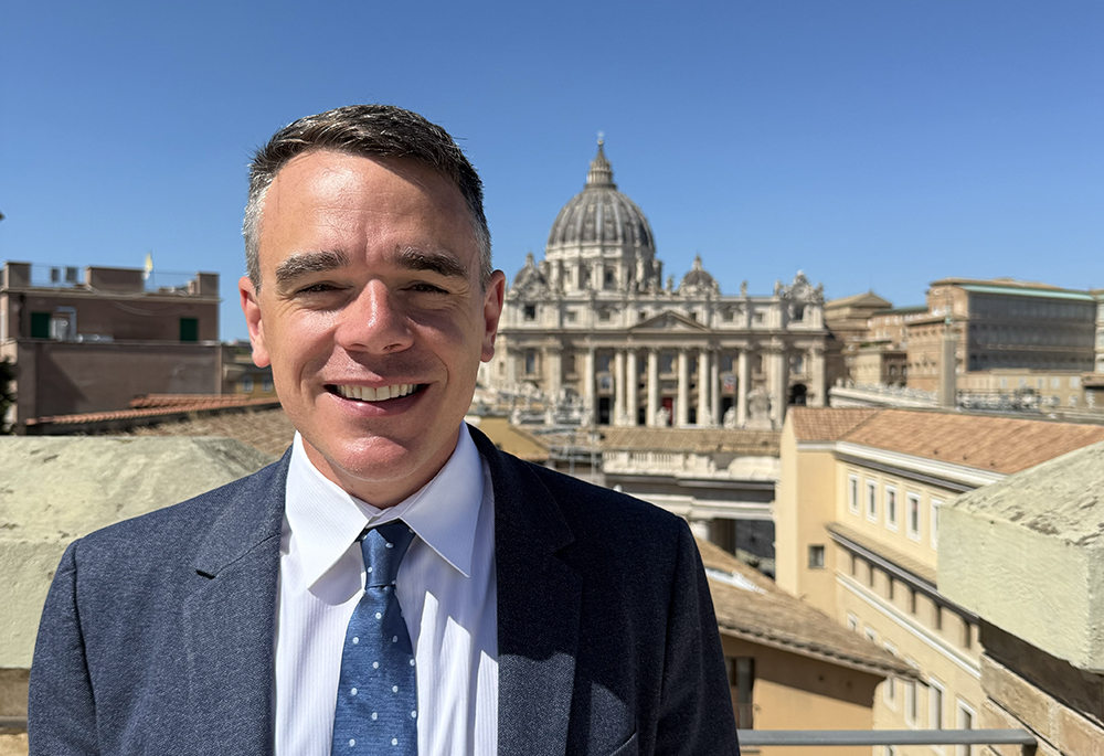 Michael J. O'Loughlin is pictured on the rooftop of the Jesuit Curia, with St. Peter's Basilica in the background, at the Vatican in September 2025. "Capturing the full range of experiences and individuals that make up the church is my goal as editor of NCR," writes O'Loughlin. (Courtesy of Michael J. O'Loughlin)