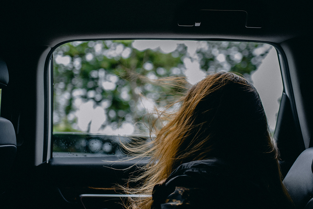 A girl looking out the window of the backseat of a car (Unsplash/Ham Kris)