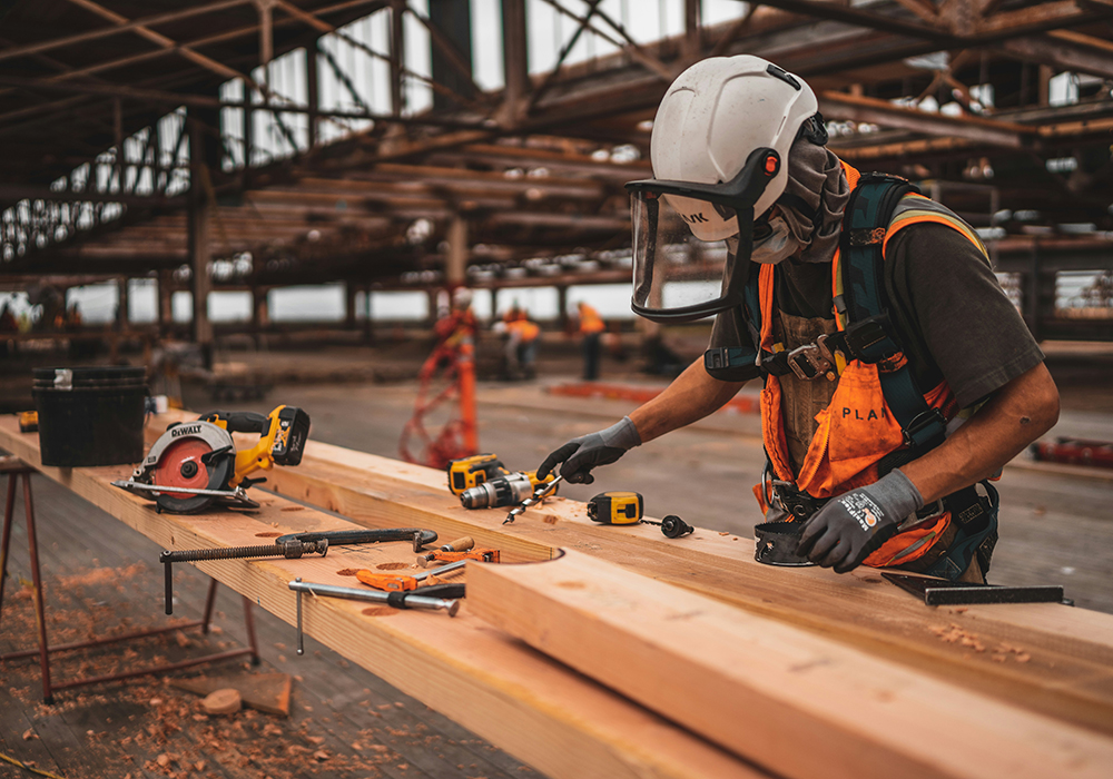 A worker uses tools on lumber at a work station in this photo illustration. (Unsplash/Jeriden Villegas)