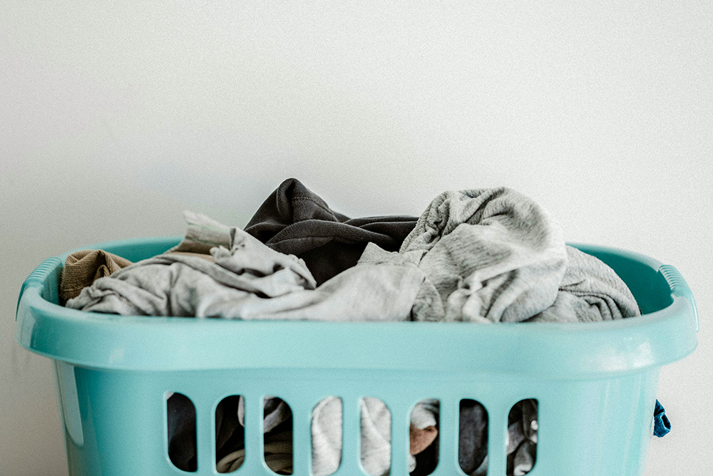A blue laundry basket filled with clothes (Unsplash/Annie Spratt)