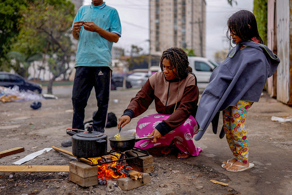 A woman burns wood on the street to cook a meal for her husband and their daughter outside their home in São Paulo Sept. 16, 2022. (OSV News/Reuters/Amanda Perobelli)