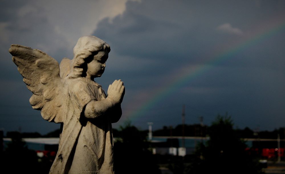 A rainbow appears in the distance near an angel grave marker following a thunderstorm at St. Patrick Catholic Cemetery in Neenah, Wisconsin. (CNS/The Compass/Brad Birkholz)