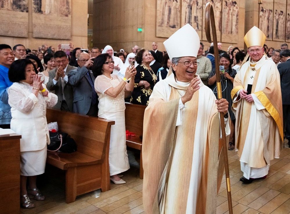 Auxiliary Bishop Alejandro "Alex" Aclan waves to the congregation during his episcopal ordination at the Cathedral of Our Lady of the Angels in Los Angeles May 16, 2019. Archbishop José Gomez is at right.  Pope Leo XIV accepted the resignation of Aclan, 75, on May 22, 2026. (OSV News/Angelus News/Victor Aleman)
