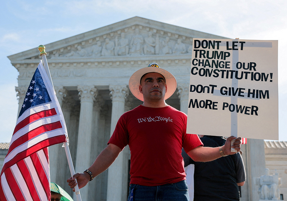 A demonstrator wearing a T-shirt with the phrase "We the people" holds a sign and a U.S. flag outside the U.S. Supreme Court in Washington April 1, 2026, on the day the court heard oral arguments on the legality of the Trump administration's effort to limit birthright citizenship. (OSV News/Reuters/Kylie Cooper)