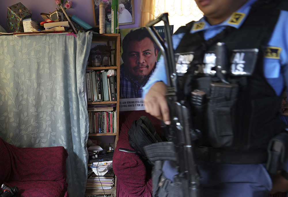 A poster of slain environmentalist Juan López hangs in his home as a state-assigned bodyguard watches over the López family, in Tocoa, Honduras, Dec. 6, 2024. (AP photo/Moises Castillo)