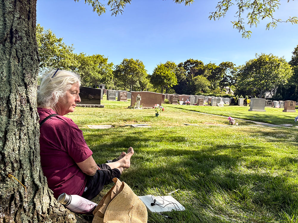 Martha Hennessy, Dorothy Day's granddaughter, sits by her grandmother's grave at Resurrection Cemetery in Staten Island, New York, June 8, 2026. (NCR photo/Camillo Barone)