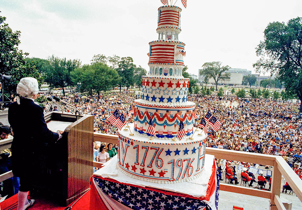 A man dressed in a period costume including powdered wig speaks to crowds while a giant cake sits beside him in Washington, D.C., July 4, 1976, during celebrations for the nation's bicentennial. (AP)