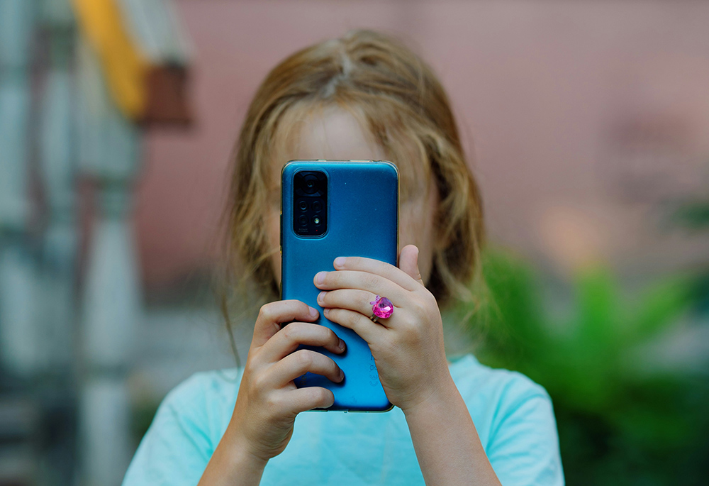 A child with a blue cellphone in front of her face (Unsplash/Andrey K.)