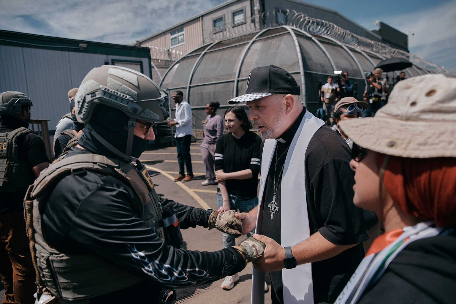 The Rev. Erich Kussman, from St. Bartholomew Lutheran Church, center, prays with a U.S. Immigration and Customs Enforcement agent outside Delaney Hall detention during a protest against the transfer of detainees, on May 26, 2026, in Newark.