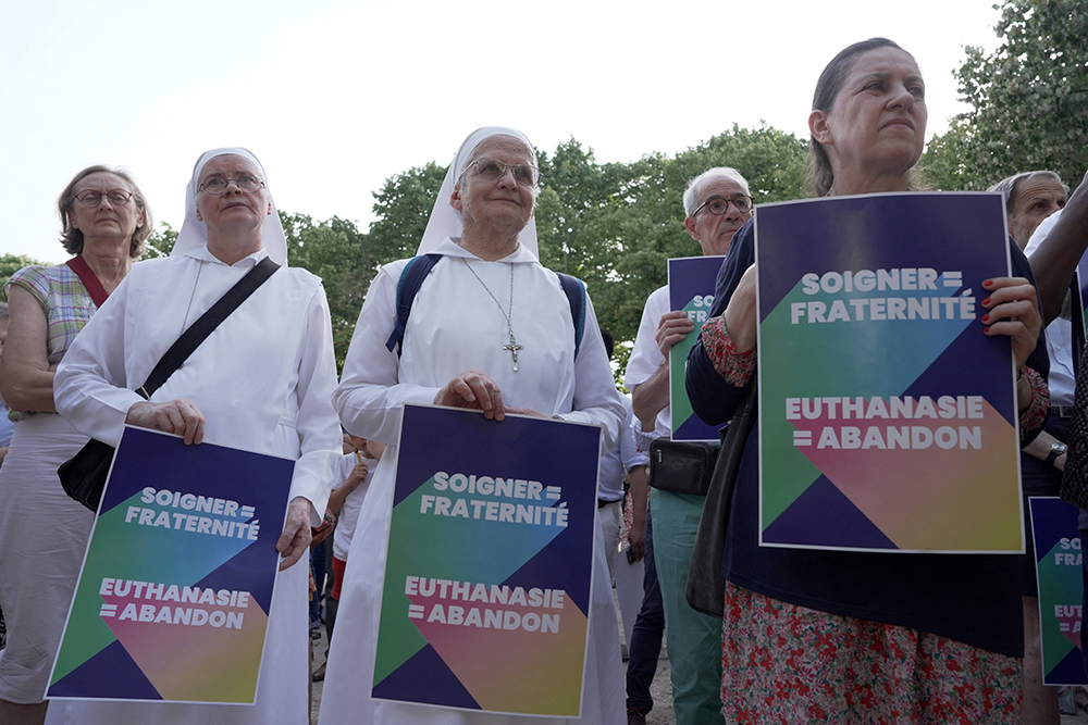 Opponents of "assisted dying" gather during a vote by members of parliament on a bill establishing the right to medical aid in dying at the National Assembly in Paris July 15, 2026. The placards read "Caring = fraternity – Euthanasia = abandonment." (OSV News/Reuters/Noemie Olive)