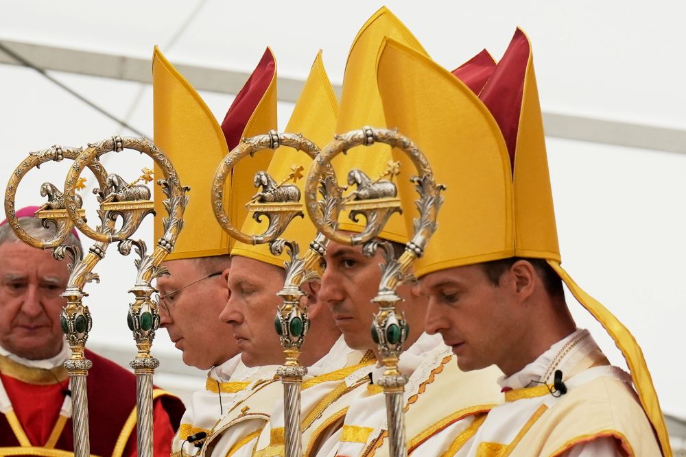 Newly consecrated bishops, from left, Pascal Schreiber, Michael Goldade, Michel Poinsinet de Sivry and Marc Hanappier, wearing their miters and holding their pastoral staffs, pray at the end of their consecration ceremony in a tent set up outside the Society of St. Pius X seminary in Écône, Switzerland, July 1, 2026. (AP/Baz Ratner)