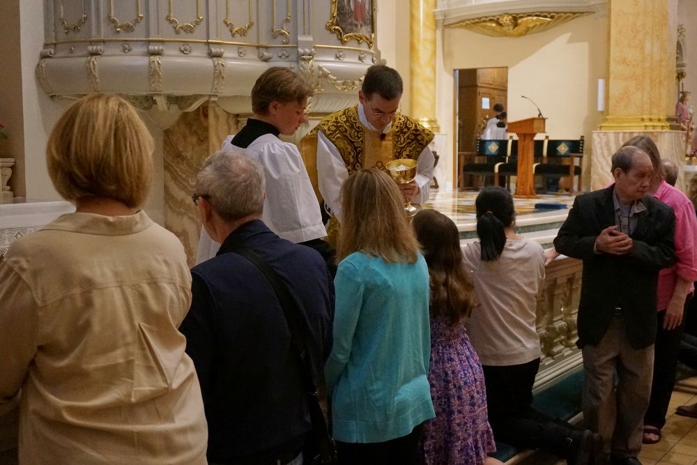 Worshippers at the Church of St. Agnes receive Communion on the tongue and while kneeling at the altar rails, in the traditional custom, during one of the Catholic parish's Latin Masses in St. Paul, Minn., June 28, 2026. (AP/Giovanna Dell'Orto)