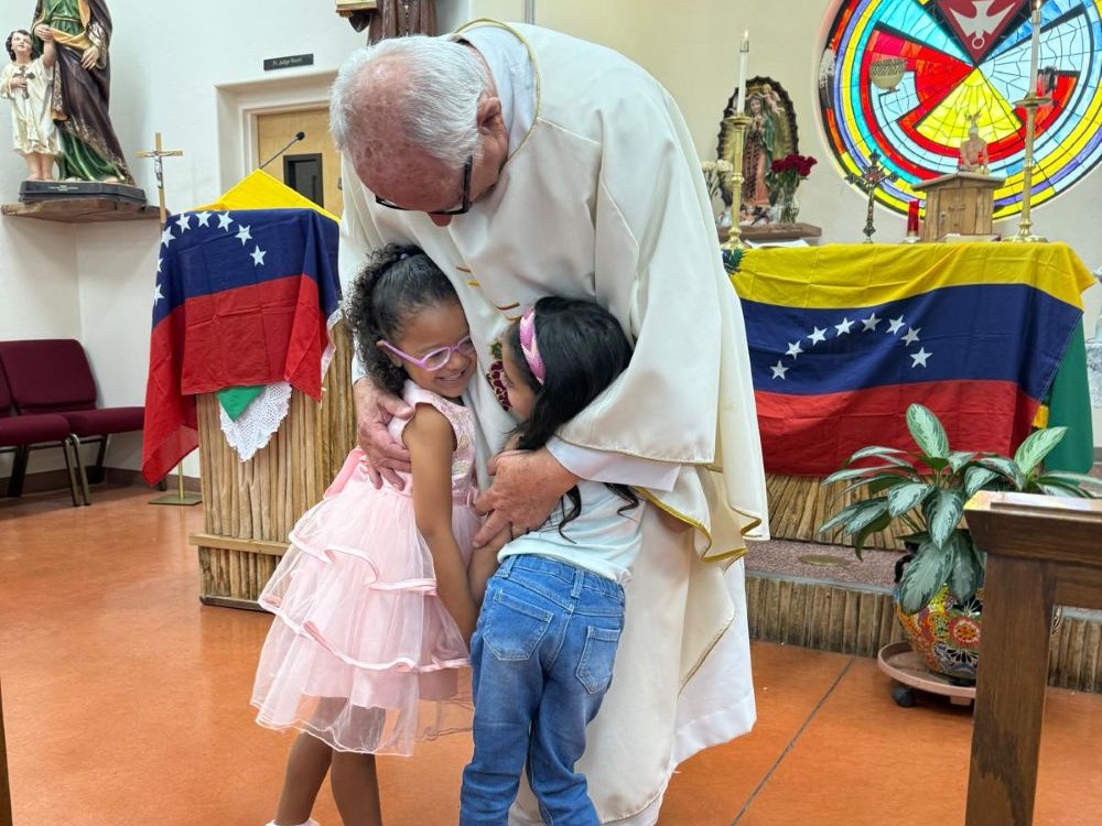 Missionary priest Fr. Raymond Riding hugs two little girls at a Mass hastily organized on June 27 in Tucson, Arizona, to support Venezuelan migrants who are worried and in mourning after two devastating earthquakes killed hundreds of people and injured thousands more in their homeland on June 24. (Anita Snow)