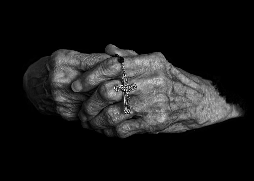 hands clasped and holding small cross/rosary