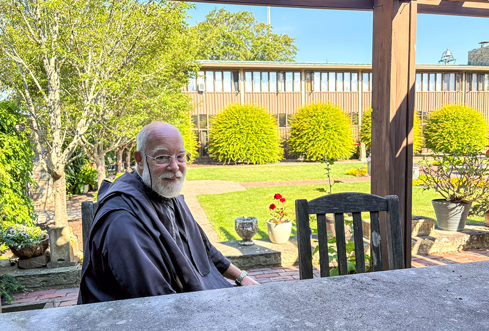 Benedictine Br. Joseph Byron, monk at Portsmouth Abbey and boarding school in Portsmouth, Rhode Island, sits in the monastery's cloister June 17, 2026. (NCR photo/Camillo Barone)