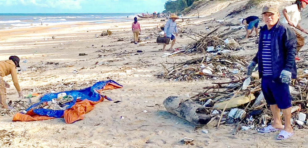 John Truong Dinh Bang, right, and parishioners collect trash along a beach in Hue, Vietnam, on June 20, 2026 as part of a parish environmental initiative. (Joachim Pham)