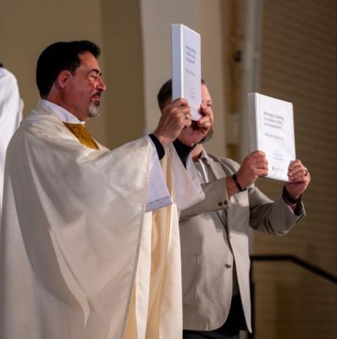 Fr. Carlos Gomez, chair of the presbyteral council at the Diocese of Phoenix, and Christoph Lohr, chair of the diocesan pastoral council, hold folders with the synodal report at the closing Mass of the synod of young adults in February. (Courtesy of Phoenix Diocese/Brett Meister)