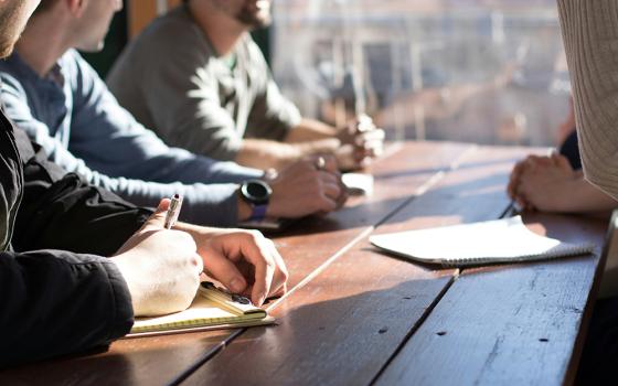 People sit with pen and paper in discussion at a table. (Unsplash/Dylan Gillis)