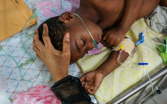 A woman caresses her child's head as he rests on a bed at the St. Damien Pediatric Hospital of Port-au-Prince, Haiti, Friday, Nov. 12, 2021. (AP/Matias Delacroix)