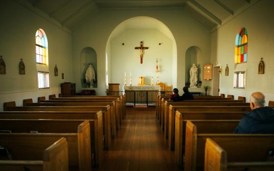 An older man sits in the back of a row of pews, facing the front of a nearly empty church. (Unsplash/Martin Jernberg)