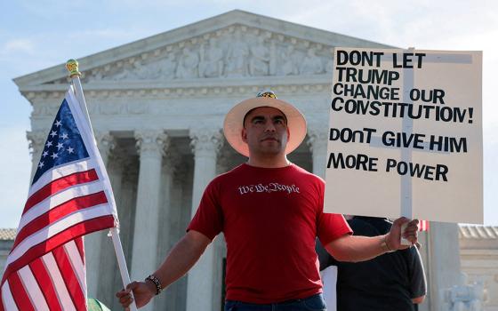 A demonstrator wearing a T-shirt with the phrase "We the people" holds a sign and a U.S. flag outside the U.S. Supreme Court in Washington April 1, 2026, on the day the court heard oral arguments on the legality of the Trump administration's effort to limit birthright citizenship. (OSV News/Reuters/Kylie Cooper)