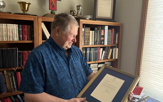 Author, composer and professor Fr. Michael Joncas holding a June 2024 letter from former U.S. president Joe Biden by the bookcase where he framed and displayed the original 1976 score of "On Eagle's Wings," in his apartment in St. Paul, Minnesota, May 2026. (NCR photo/Camillo Barone)