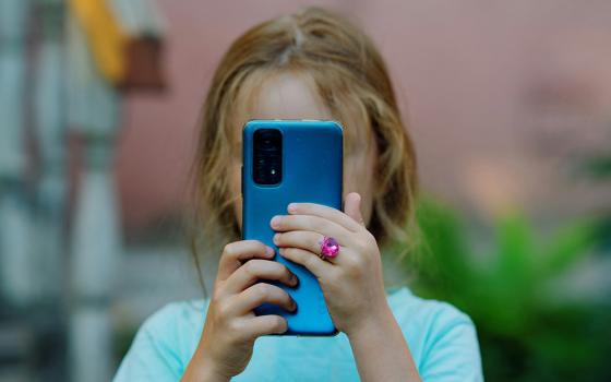 A child with a blue cellphone in front of her face (Unsplash/Andrey K.)