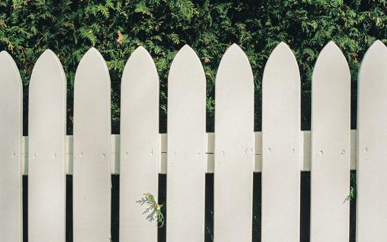 A whitewashed wooden fence in front of evergreen trees (Unsplash/Lawrence Krowdeed)