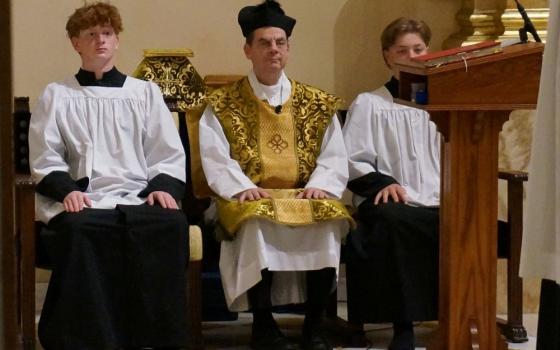 Fr. John Ubel, pastor of the Church of St. Agnes, wears the traditional biretta hat and vestments as he sits between altar servers during one of the Catholic parish's Latin Masses in St. Paul, Minn., June 28, 2026. (AP/Giovanna Dell'Orto)
